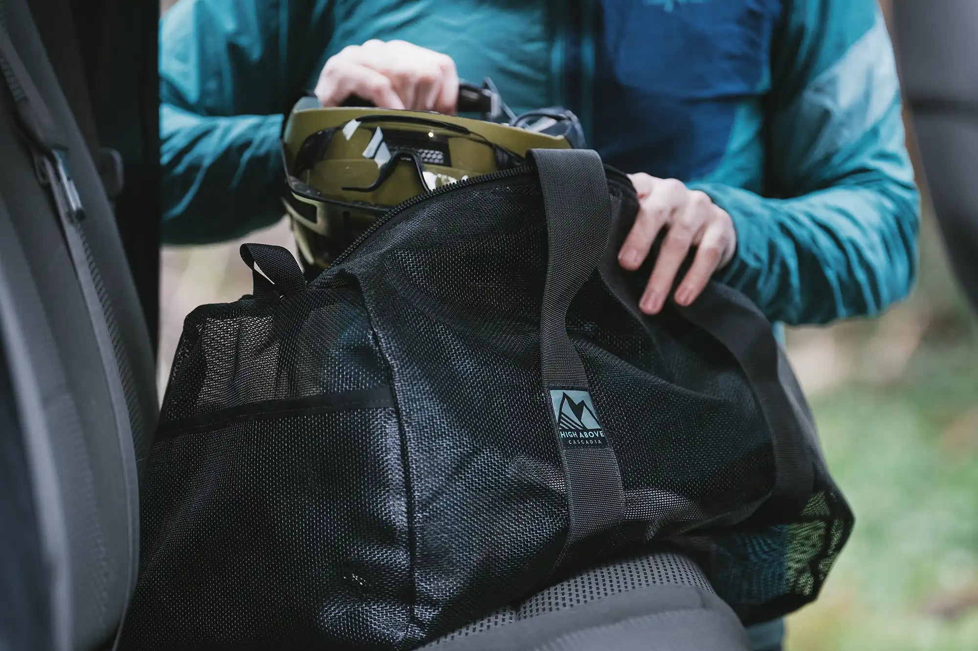 Person loading helmet into High Above Lost Lake Duffel Bag in back seat of vehicle.