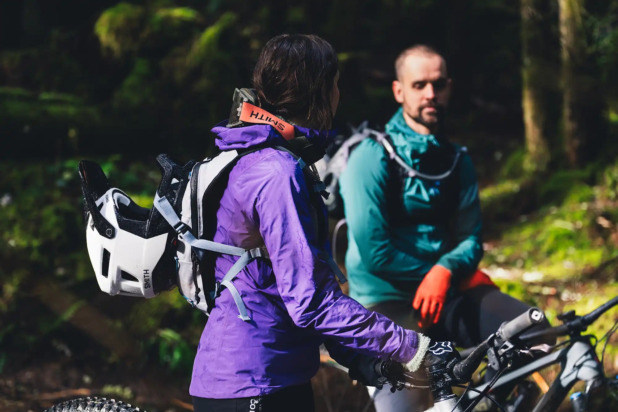 Two mountain bikers wearing High Above Supernatural Hydration Vest Pack with full face helmets attached.