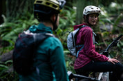 Two mountain bikers in the forest talking while wearing High Above Supernatural Hydration Vest Packs