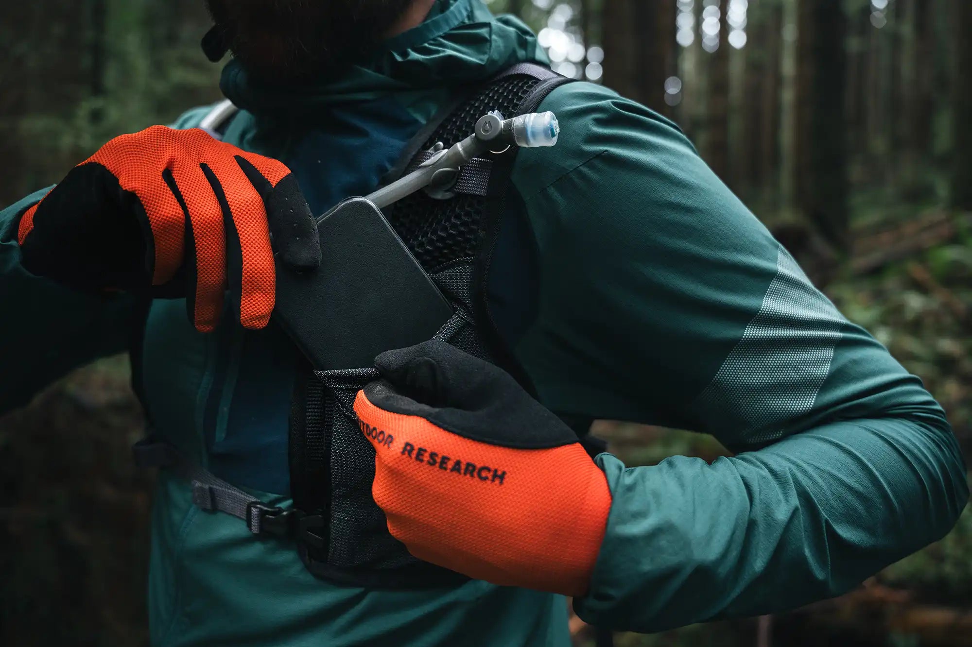 Close up of person putting smartphone into front stretch pocket on High Above Supernatural Hydration Vest Pack