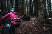Mountain bike rider wearing High Above Venture hip pack riding through forest.