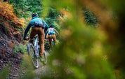 Two mountain bike riders wearing high above venture hip packs riding through forest