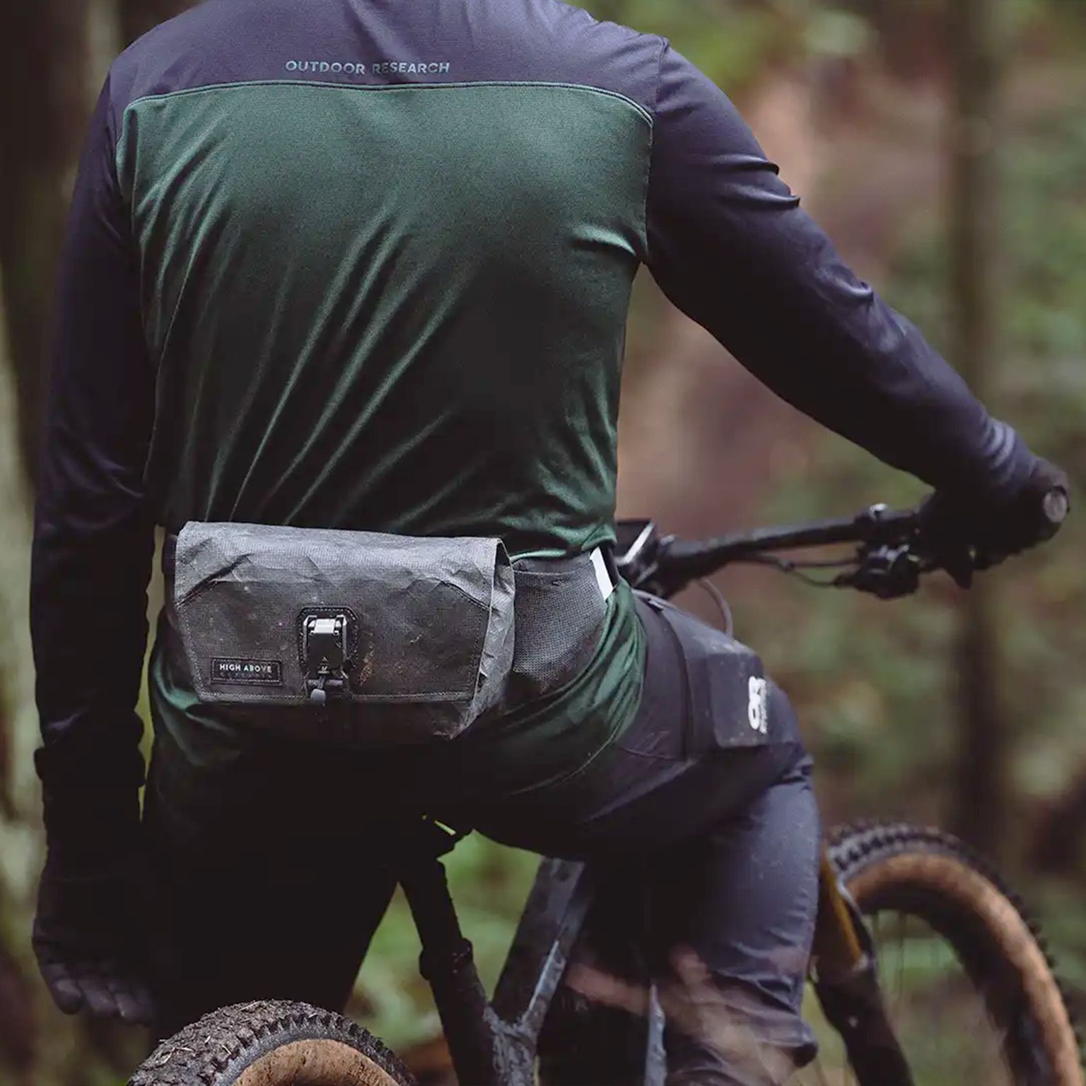 Person riding a bike with a High Above Venture 3D hip pack in a forest setting